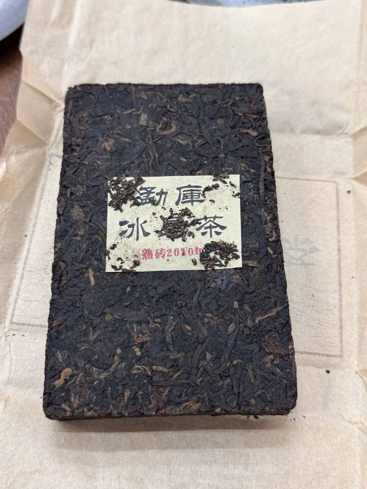 A dark pressed tea brick with a paper label reading 勐库冰岛茶 and 熟砖2010年